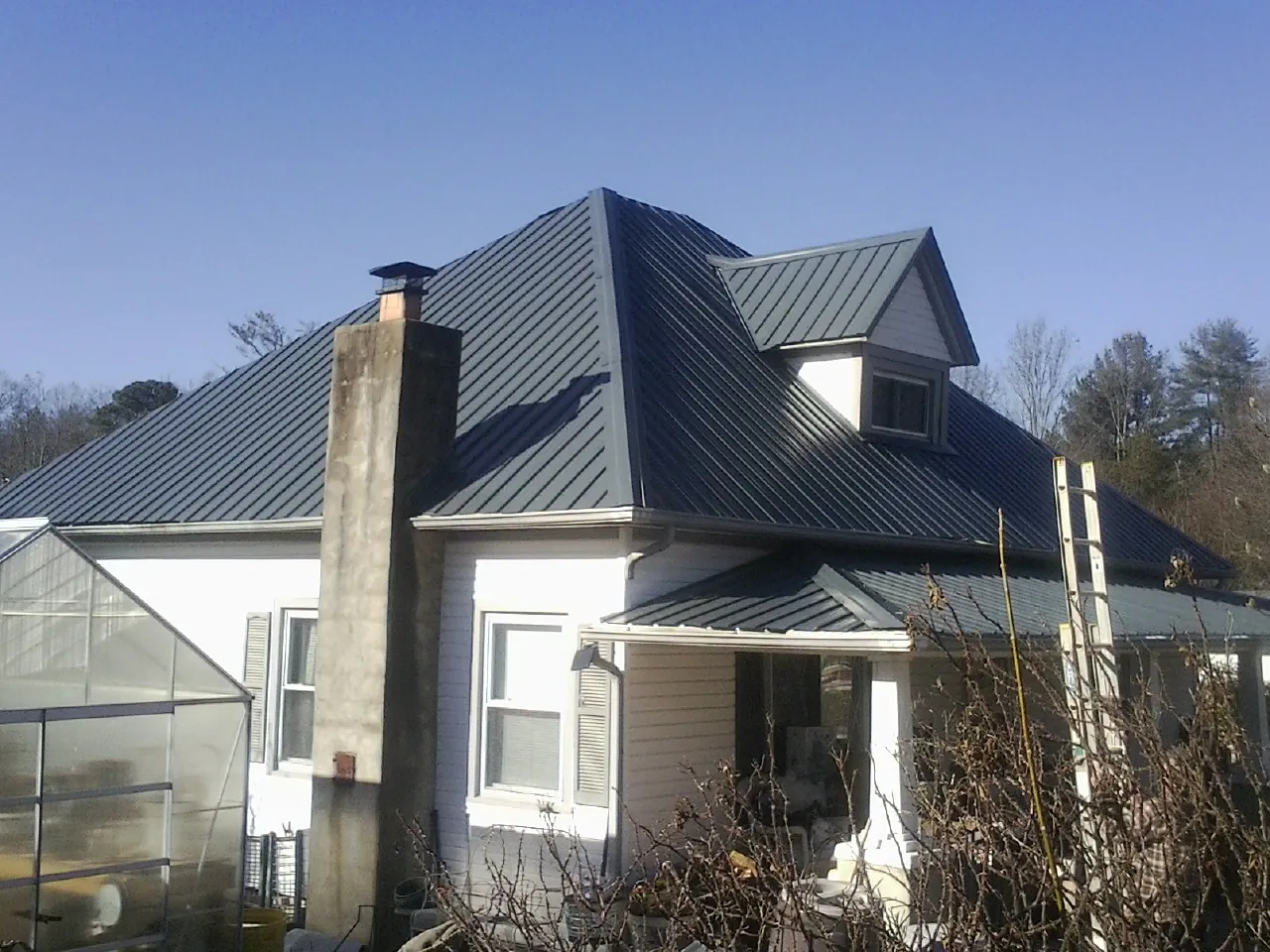 Dark blue standing seam metal roof on a white farmhouse with dormer — Slate & Tile Roof Repair by Roofing Brothers in Greeley