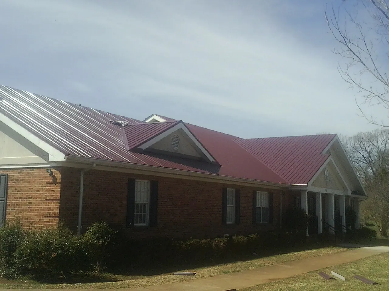 Red metal roof with gabled entries on a long brick building, from a Hail Damage Roof Repair job in Greeley