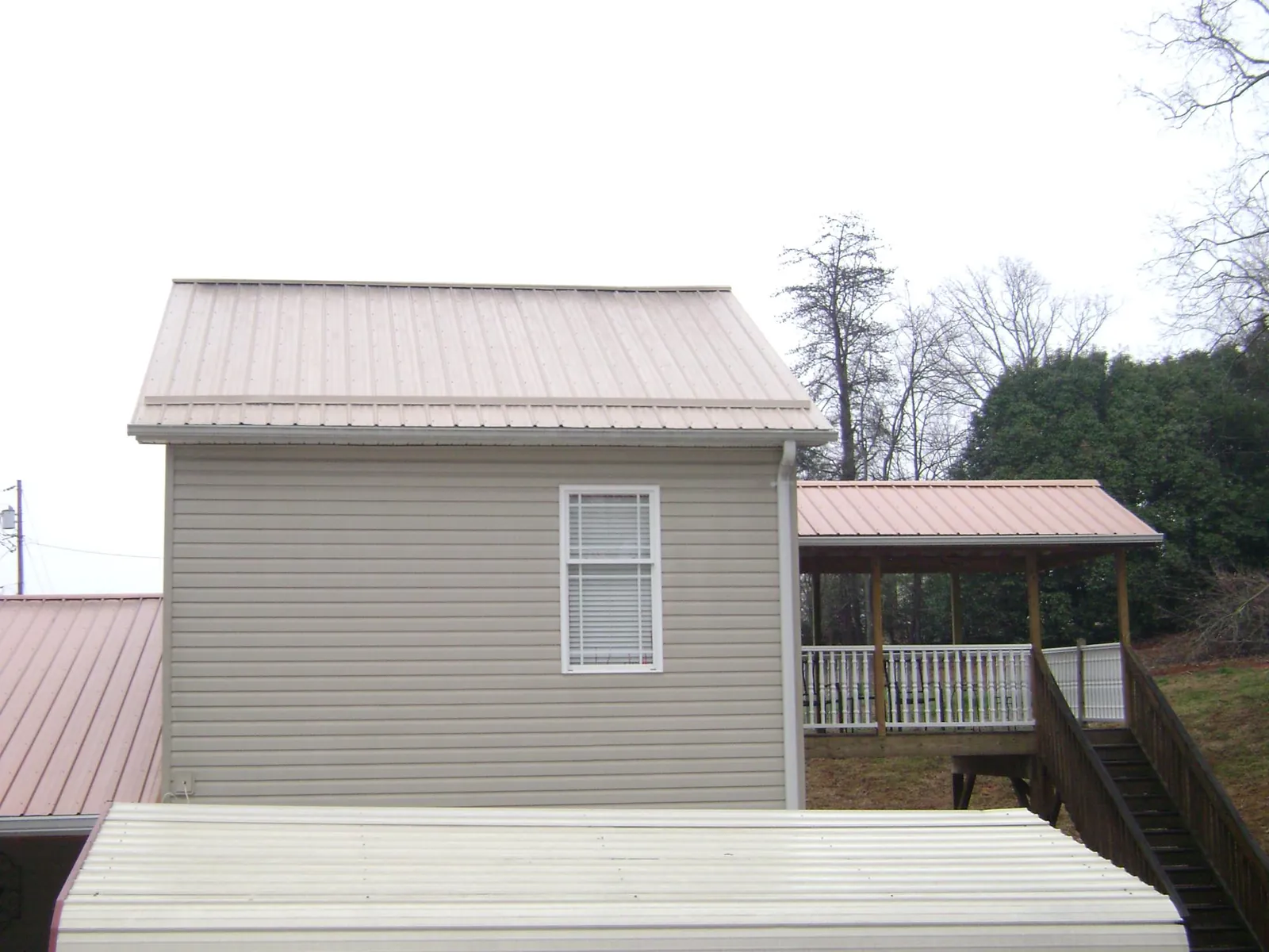 Tan metal roofs on a two story addition and attached porch, from a Roof Replacement job in Greeley
